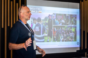Man with a lanyard presenting in front of a projector screen at Sea Otter Australia