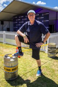 Smiling man in a navy shirt with his foot on a beer keg on the grass