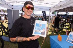 Man in a black cap and sunglasses holding a sign under an expo tent