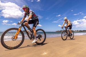 Two mountain bikers riding along the sand on a beach