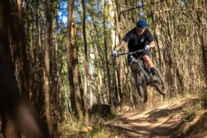 Mountain biker launching off a jump between tall forest trees