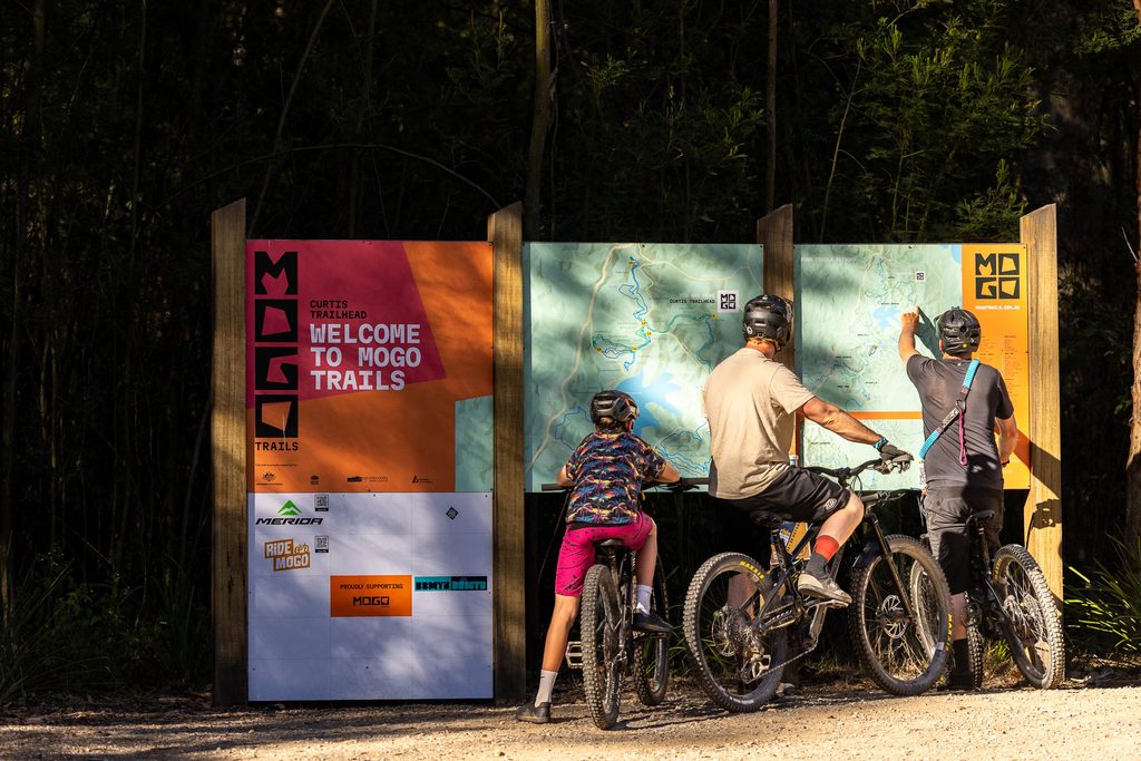 Three riders with their bikes reading the Mogo Trails welcome map