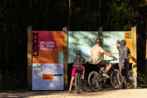 Three riders with their bikes reading the Mogo Trails welcome map