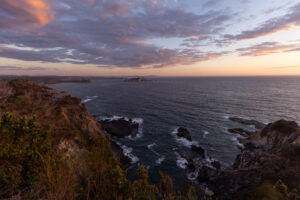 Waves breaking over a rocky coastline under a colourful sunset sky