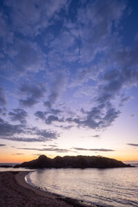 Purple and orange sunset sky above a headland and a quiet beach